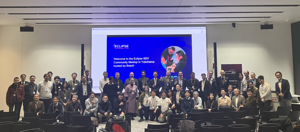 Large group photo of attendees at the Eclipse SDV Community Meetup in Yokohama, standing and kneeling in a conference room. Behind them, a presentation screen reads ‘Welcome to the Eclipse SDV Community Meetup in Yokohama hosted by Bosch,’ with the Eclipse Foundation logo displayed.