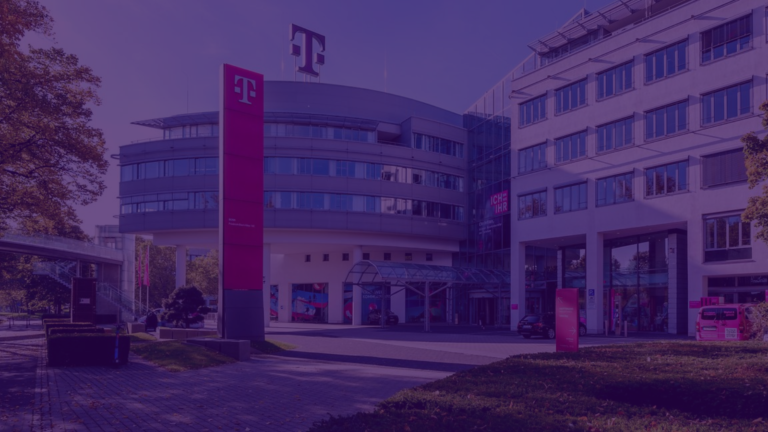 Exterior view of the T-Systems campus building in Bonn, Germany. The modern office complex features curved glass façades, a prominent magenta T-Systems logo sign in the foreground, and surrounding trees and walkways, shown with a purple color overlay.