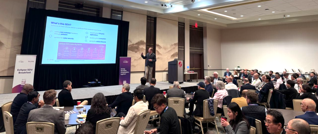 Man giving a presentation on stage in front of an audience at CES, looking at a presentation slide.