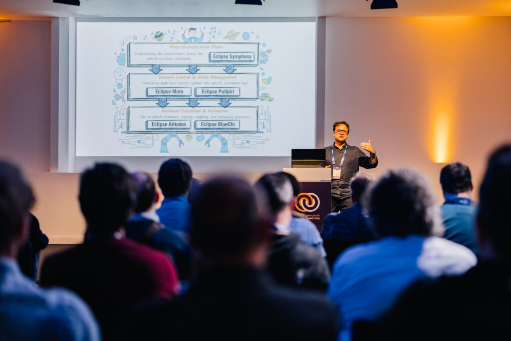 A man presenting in front of an audience on stage at Open Community for Automotive