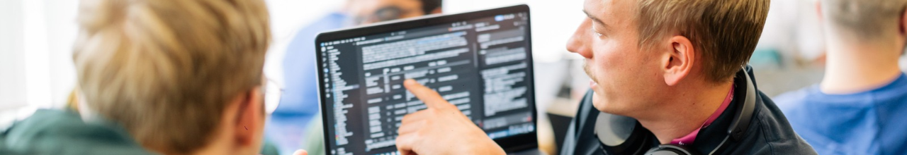 Two men looking at a laptop screen on which there is code