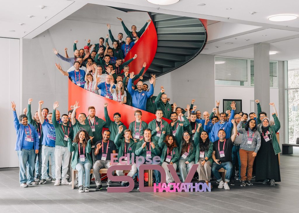 A large group of people standing in a hallway, waving at the camera at the Eclipse SDV Hackathon 2026.