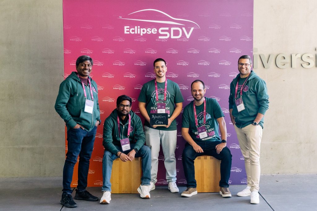 Group of five people standing and sitting in a row in front of an Eclipse SDV branded background, facing the camera, wearing lanyards