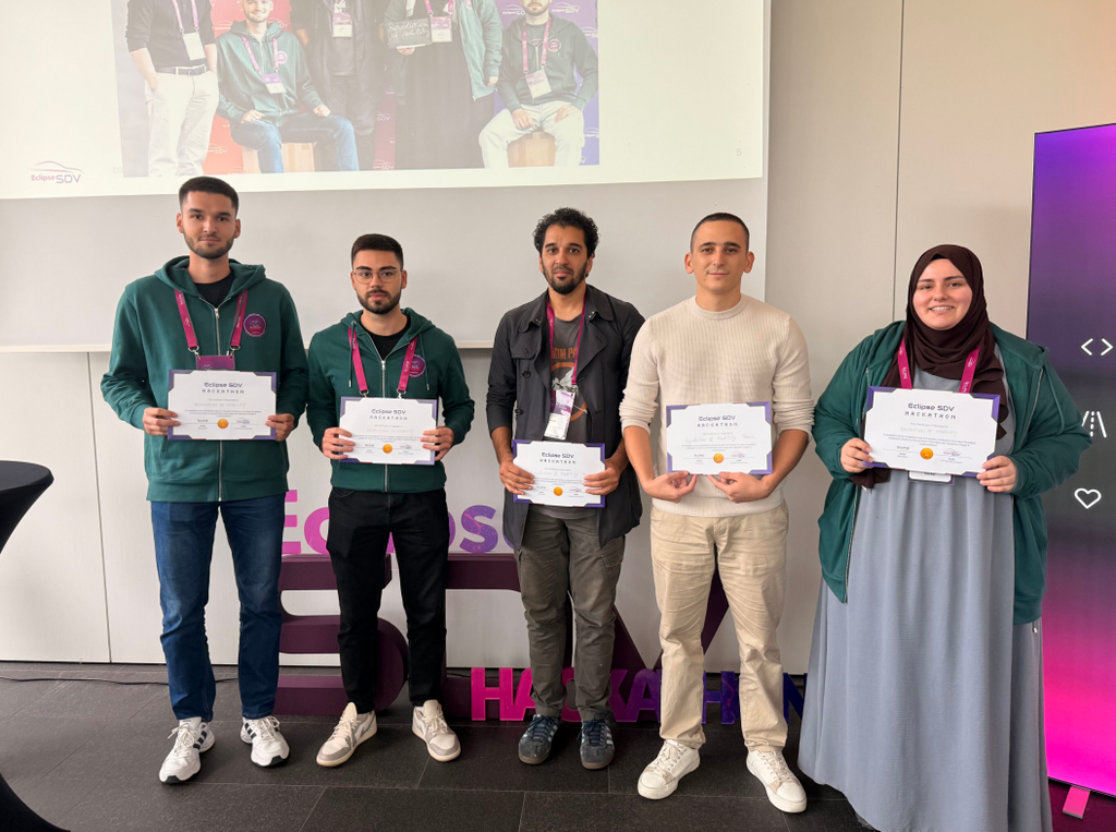 Group of five people standing in a row facing the camera, all of them holding winners certificates in their hands
